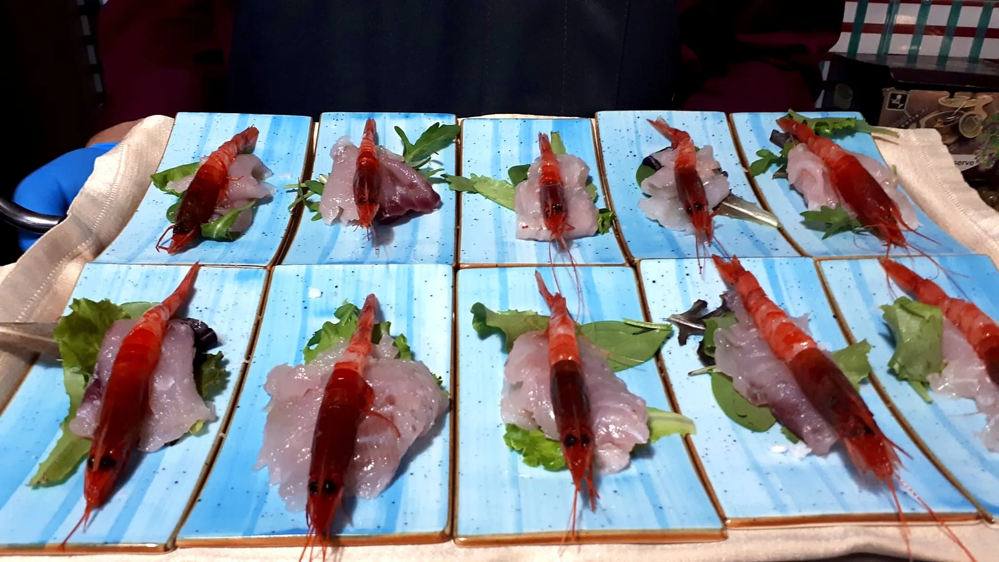 Piatti azzurri con pesce crudo e un gambero rosso ciascuno