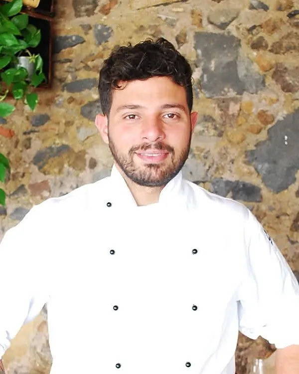 Lo chef Dario Finocchiaro, in giacca bianca, davanti a un muro di pietra lavica